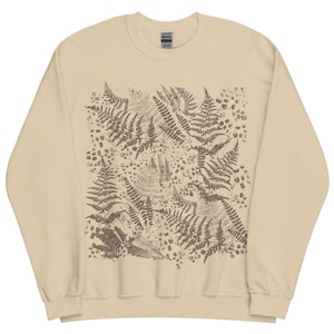 Puede incluir: Sudadera beige con un estampado de helechos marrones. El dise&ntilde;o es un patr&oacute;n repetido de ilustraciones detalladas de helechos, creando un tema natural y bot&aacute;nico. La sudadera tiene cuello redondo y mangas largas, adecuada para uso casual.