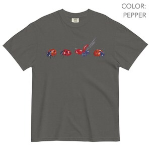 May include: Dark grey t-shirt with a watercolour illustration of ladybirds. The ladybirds are red with black spots and are set against a dark grey background. The shirt has a crew neck and short sleeves. The colour is 'pepper'.