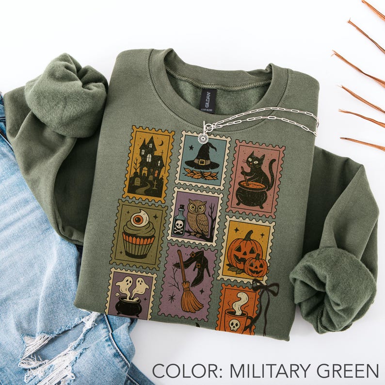 Pu&ograve; includere: Felpa verde militare con un design a timbro a tema Halloween. I timbri presentano una casa infestata, un cappello da strega, un gatto nero, un cupcake, un gufo, una zucca, fantasmi, una scopa e un teschio con caff&egrave;. Una collana d'argento &egrave; drappeggiata sulla felpa.