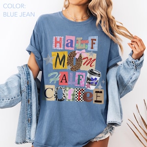 May include: Blue jean colored t-shirt with the text "Half Mom Half Coffee". The text is in a variety of patterns and colors, including plaid, leopard print, and a coffee cup graphic. The shirt has rolled-up sleeves.