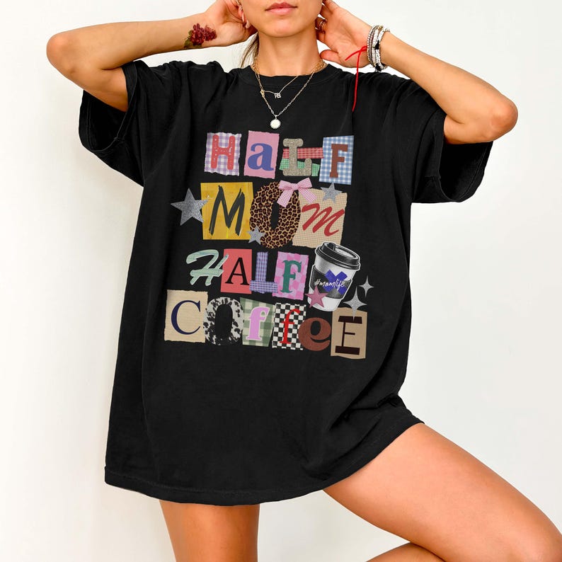 May include: Black t-shirt with the text "Half Mom Half Coffee" in a colorful, patchwork design. The design includes a coffee cup graphic and star accents. The shirt is a casual, oversized fit.