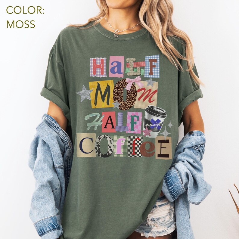 May include: Moss green t-shirt with the text "Half Mom Half Coffee" in a colorful, block letter design. The design includes a coffee cup graphic and a bow with a leopard print pattern. The shirt is a relaxed fit.