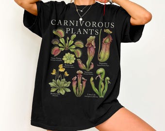 Può includere: T-shirt nero con un'illustrazione botanica di piante carnivore, tra cui dionee e piante a brocca. Il testo "CARNIVOROUS PLANTS" è stampato in bianco. La maglietta ha una vestibilità ampia.
