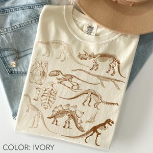 レトロな恐竜の骨格シャツ Comfort Colors、ヴィンテージ化石落書きシャツ、先史時代の骨のグラフィックTシャツ、古生物学シャツ、恐竜好きへのギフト