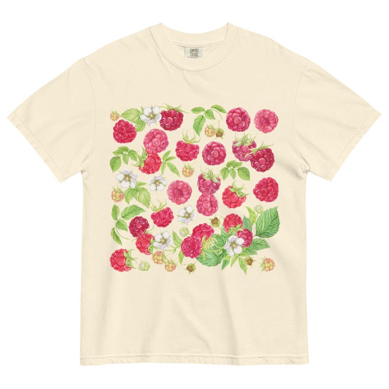 Op de afbeelding: Cr&egrave;mekleurig T-shirt met een aquarelontwerp van frambozen, groene bladeren en witte bloemen. De frambozen zijn in verschillende tinten rood en roze. Het ontwerp is over de voorkant van het shirt verdeeld.