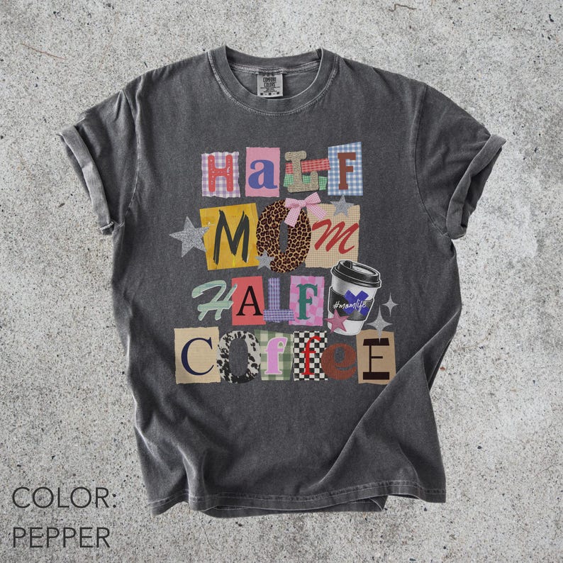 May include: Pepper-colored t-shirt with the text "Half Mom Half Coffee" in a patchwork design. The design includes a coffee cup graphic and star accents. The shirt is a crew neck and has rolled-up sleeves.