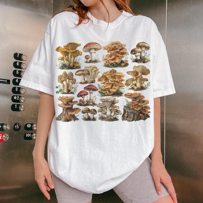 Pu&ograve; includere: T-shirt bianco con un'illustrazione dettagliata di vari funghi nei toni del marrone, rosso e giallo. Il design presenta una variet&agrave; di funghi, creando un tema botanico. La maglietta ha una vestibilit&agrave; casual e oversize.