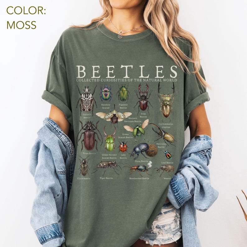 Puede incluir: Camiseta verde musgo con una ilustraci&oacute;n detallada de varios escarabajos con sus nombres. El texto "BEETLES COLLECTED CURIOSITIES OF THE NATURAL WORLD" est&aacute; impreso en la parte superior. La camiseta es de corte holgado.