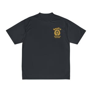 May include: Dark grey athletic t-shirt with short sleeves. The shirt has a gold logo on the upper left chest. The logo says "BeeFit" above a lion's head design. Below the logo is the text "BattleGround Socal 2026".