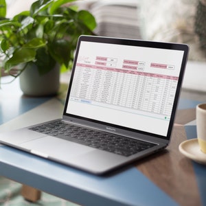 May include: A laptop computer with a spreadsheet open on the screen. The spreadsheet is titled "Milk Tracker" and contains columns for date, milk type, quantity, and price. The laptop is sitting on a blue table with a cup of coffee and a plant in the background.