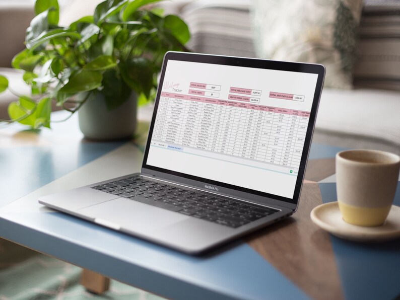 May include: A laptop computer with a spreadsheet open on the screen. The spreadsheet is titled "Milk Tracker" and contains columns for date, milk type, quantity, and price. The laptop is sitting on a blue table with a cup of coffee and a plant in the background.