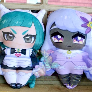 May include: Two plush dolls with anime-style features. One doll has teal hair and a maid outfit, the other has lavender hair and a purple dress. Both dolls have large eyes and are made of soft fabric.