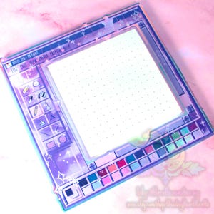 Puede incluir: Un bloc de notas de acrílico transparente con un diseño que simula una interfaz de programa de pintura informática. El bloc de notas presenta una cuadrícula punteada blanca, una paleta colorida e iconos. El texto "NOTES.JPG - BH PAINT" es visible.