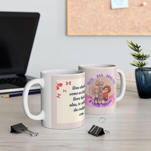 Puede incluir: Dos tazas de cerámica blanca con asa. Una taza presenta texto y gráficos de mariposas, la otra tiene un gráfico de una anciana y dos niños con texto. Las tazas están sobre una superficie clara.
