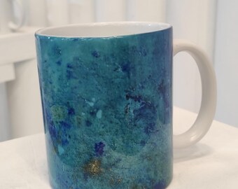 Puede incluir: Una taza de cerámica azul y dorada con un diseño moteado. La taza tiene un asa blanca y un interior blanco.