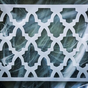 May include: White plastic stencil with a geometric pattern of repeating arches and stars. The stencil is designed for crafting and decorating projects.