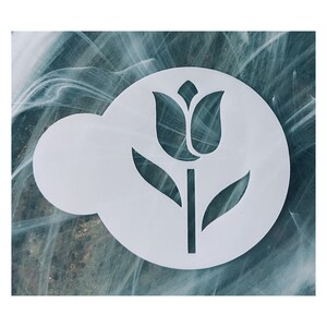 May include: A white, circular stencil featuring a tulip design. The stencil has a flower with two leaves and a stem. The background is a marbled pattern of teal, white, and gray.