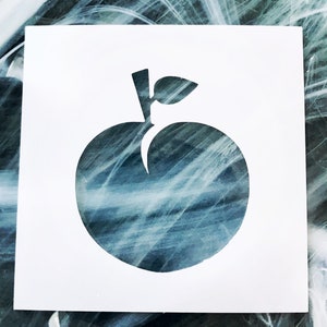May include: A white stencil of an apple with a leaf on top. The stencil is on a blue and white background.