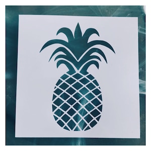 May include: A white stencil of a pineapple with a dark teal outline. The pineapple is shown with a detailed design of the leaves and the fruit.