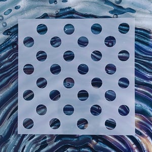 May include: A square, semi-transparent stencil featuring a repeating grid pattern of circular cutouts. The stencil is positioned over a background with swirling, iridescent colors including deep blues, purples, and metallic silver tones.