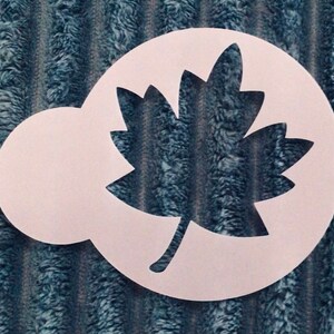May include: White plastic stencil of a maple leaf with a handle. The stencil is designed for crafting and decorating.