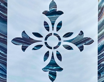 May include: A square white stencil featuring a central cutout design of a symmetrical four-pointed floral motif. The pattern consists of four stylized petals radiating from a circular center, with each point ending in a fleur-de-lis shape.