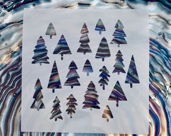 May include: A square white stencil featuring multiple cutouts of pine trees in various sizes. The stencil is placed over a background with a swirling, marbled pattern of metallic blue, purple, silver, and bronze colors visible through the tree shapes.