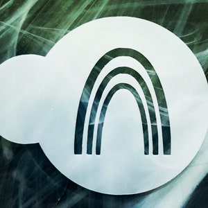 May include: White plastic stencil with a black rainbow design. The stencil is shaped like a cloud.