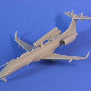 Può includere: Un modello in plastica grigia di un piccolo jet privato con un radar sul tetto. Il modello è su uno sfondo blu.