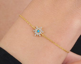 Può includere: Un braccialetto a catena dorata con un ciondolo a forma di fiocco di neve. Il fiocco di neve è decorato con pietre trasparenti e turchesi.