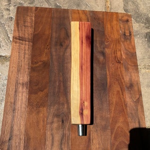 May include: A wooden beer tap handle with a light brown and reddish-brown wood grain pattern. The handle has a metal tap at the bottom.