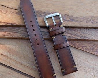 May include: A brown leather watch strap with a silver buckle. The strap has visible stitching in a lighter brown color. The leather has a distressed look.