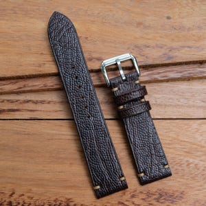 Puede incluir: Dos correas de reloj de cuero marrón con hebilla plateada. Las correas tienen una superficie texturizada y están cosidas con hilo marrón claro.