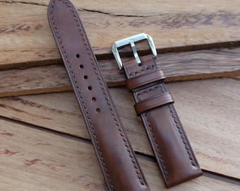 May include: A brown leather watch strap with a silver buckle. The strap has decorative stitching along the edges and several holes for adjustment. The leather appears to be high-quality and durable.