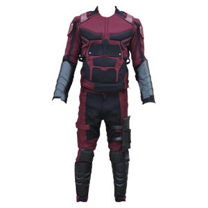 Pode incluir: Um traje de super-herói completo em bordô e preto. O traje inclui uma jaqueta com acolchoamento preto, calças combinando e protetores de antebraço e caneleiras pretas. O traje é projetado para se assemelhar a um personagem de quadrinhos.