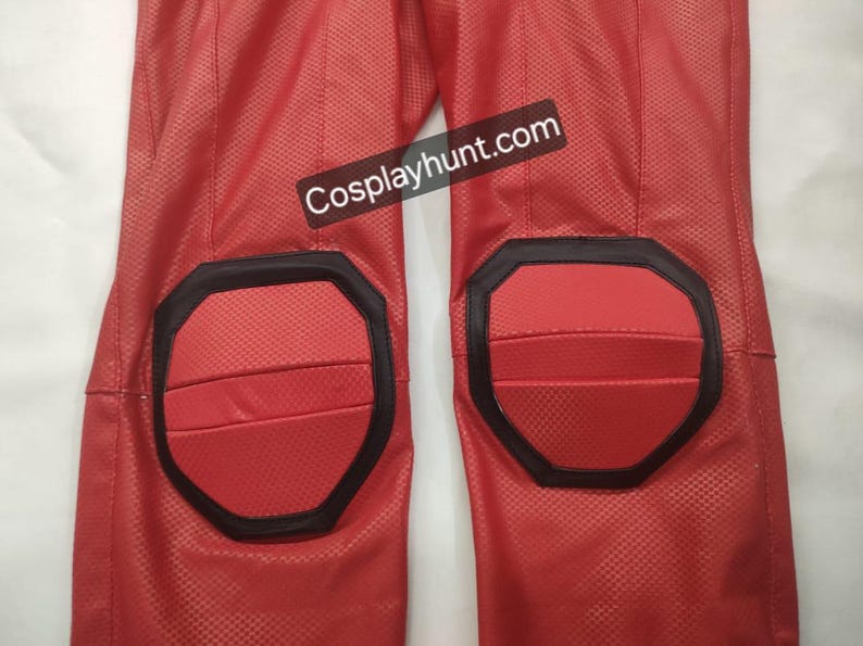 Pu&ograve; includere: Primo piano di pantaloni rossi di un costume con dettagli neri intorno alle ginocchiere. I pantaloni hanno un motivo strutturato e il testo "Cosplayhunt.com" &egrave; visibile.