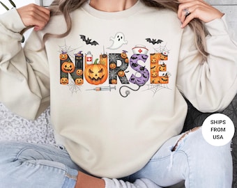 May include: A sand-colored sweatshirt with a Halloween-themed design. The word "NURSE" is spelled out with pumpkins, bats, a ghost, and a nurse's cap. A syringe and spiderwebs are also included in the design.