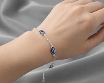Puede incluir: Una pulsera de plata con tres amuletos azules en forma de ojo, unidos por una fina cadena. Cada amuleto está adornado con pequeñas piedras azules brillantes. La pulsera se muestra sobre un fondo gris claro.