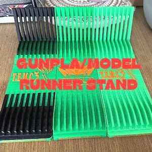 Puede incluir: Un soporte para corredores de modelos de tres secciones. El soporte es principalmente verde con detalles en negro. El texto "GUNPLA MODEL RUNNER STAND" está impreso en rojo en el soporte. Está diseñado para sujetar piezas de kits de modelos.