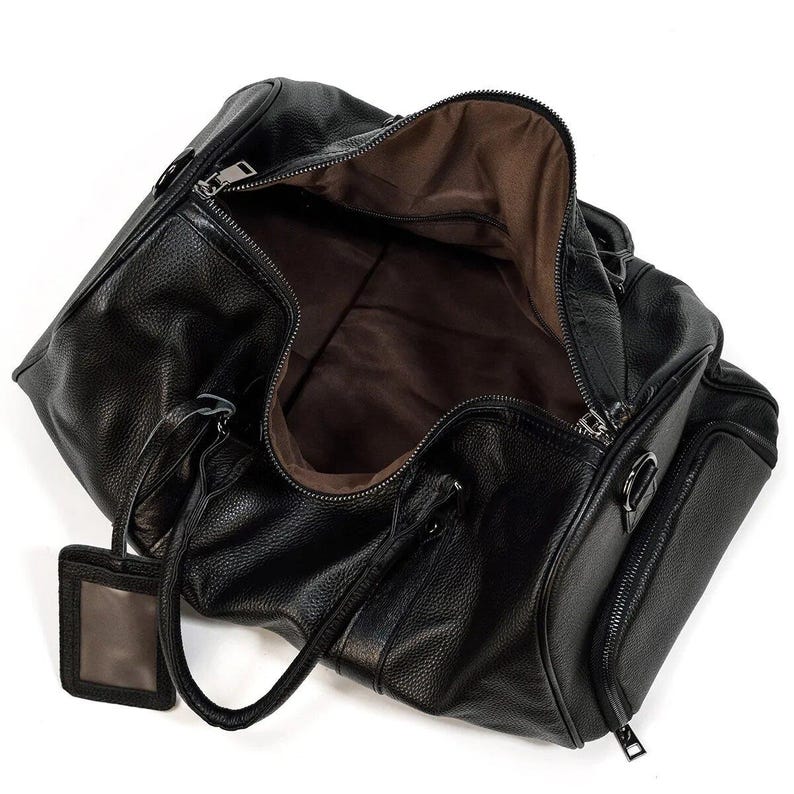 Pu&ograve; includere: Borsa da viaggio in pelle nera con chiusura a zip e una piccola tasca sul davanti. La borsa &egrave; aperta e l'interno &egrave; foderato in tessuto marrone.