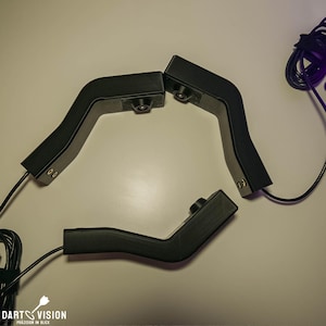 Puede incluir: Cuatro soportes de cámara negros con un diseño curvo y un pequeño botón en uno de los soportes. Los soportes están conectados por cables.