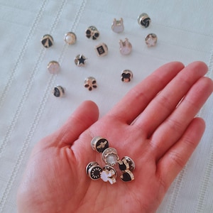 Puede incluir: Una colección de pequeños pines decorativos con varios diseños, incluyendo una abeille, una flor, una estrella, un conejo y el número "5". Los pines son de color dorado con detalles en negro y blanco.