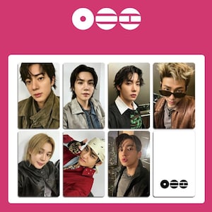 Può includere: Un set di otto fototessere con immagini di star della musica pop maschili. Le carte sono disposte in una griglia su uno sfondo rosa. La parte superiore dell'immagine presenta un logo con tre forme bianche. Le carte presentano varie pose e abiti.