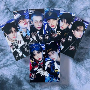 Może przedstawiać: Kolekcja prostokątnych kart fotograficznych Stray Kids z portretami poszczególnych członków. Każda karta przedstawia portret członka, a niektóre karty zawierają tekst, np. imiona i numery członków. Karty mają błyszczące wykończenie.