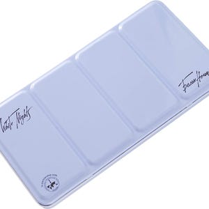 Pode incluir: Uma paleta de tinta aquarela de metal azul claro com três poços. A paleta tem o texto "White Nights" e "Daniel Smith" impresso nela.