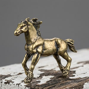 Peut inclure: Une figurine de cheval de couleur bronze en mouvement. La sculpture présente une surface texturée et des détails complexes, notamment une crinière et une queue fluides. Le cheval est posé sur une surface en bois vieilli peinte en blanc.
