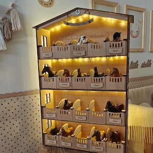 May include: A four-tiered wooden horse stable display shelf featuring individual stalls with nameplates for toy horses. The structure is illuminated by integrated warm LED string lights along the top of each level and has a peaked roof design.