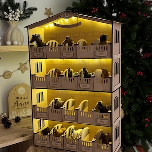 Op de afbeelding: Een houten paardenstal-displayplank met vier niveaus en geïntegreerde warme LED-verlichting. Elk niveau is voorzien van individuele stallen met kleine naamplaatjes, waarin diverse miniatuur paardenfiguurtjes zijn geplaatst.