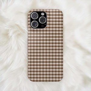 Puede incluir: Una funda rectangular para smartphone con un patrón de cuadros vichy en color marrón y blanco. La funda tiene un recorte en la esquina superior izquierda para un sistema de triple cámara, con un módulo negro que alberga tres lentes.