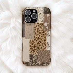 May include: A smartphone case featuring a patchwork design of various floral patterns in shades of brown, beige, and cream. The rectangular case has a cutout for a triple-lens camera system on the top left corner and a smooth, flat surface.